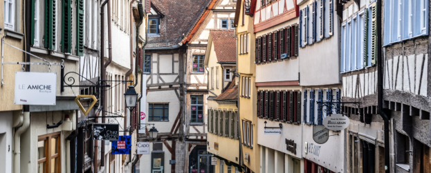 Enge Straße in Colmar, Elsass, Frankreich, gesäumt von Gebäuden auf beiden Seiten mit Fenstern, Schildern, Lichtern, Rohren und anderen Details, mit einer Straße unten.