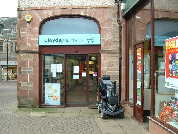 Apothekenladen mit einem vor dem Gebäude geparkten Fahrzeug und einem Gebäude in der linken Ecke.