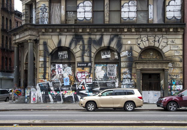 Gebäude mit Graffiti, Gittern, Treppen, Geländern, einem Himmel-Hintergrund und Fahrzeugen auf der Straße.