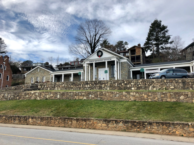 Steinwand mit geparkten Autos, benachbarten Gebäuden, Bäumen und einem bewölkten Himmel, als Weltkulturerbe-Museum bezeichnet.