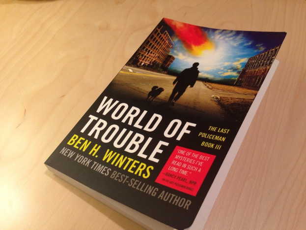 Ein Buch mit dem Titel "World Of Trouble" mit einem Bild eines Mannes und eines Hundes darauf, das auf einem Tisch liegt.