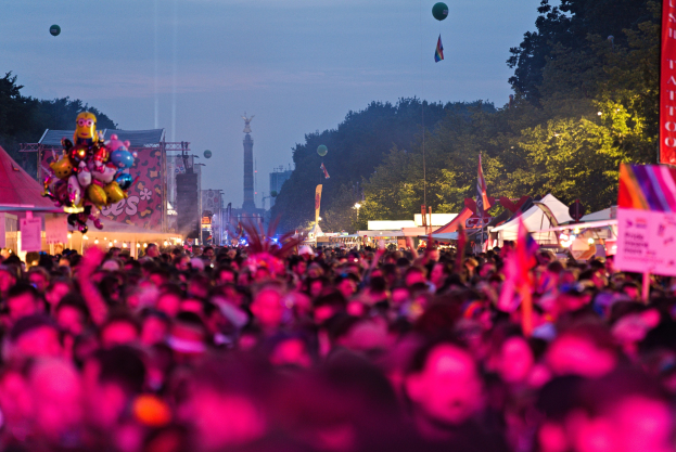 Eine große Menschenmenge auf einem nächtlichen Musikfestival, beleuchtet von bunten Lichtern und Ballons, mit Zelten, Bannern, Fahnen, Bäumen, einem Turm und einem sternenklaren Himmel im Hintergrund.