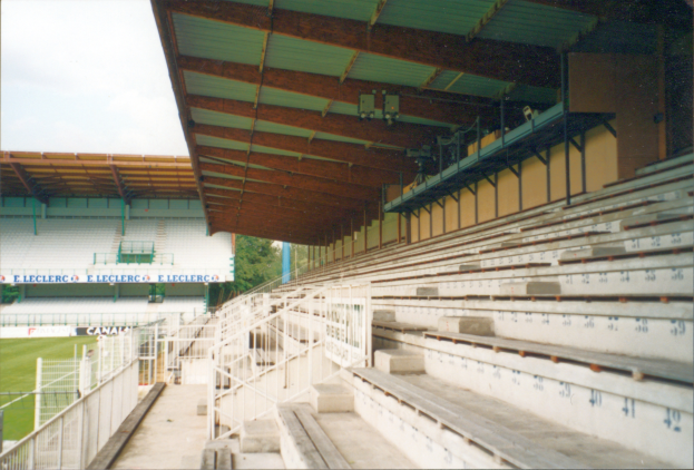 Ein altes Foto eines Stadions mit zahlreichen Sitzplätzen, Geländern, Treppen, einem Schuppen, Texttafeln, Gras, Bäumen und einem Himmel im Hintergrund.