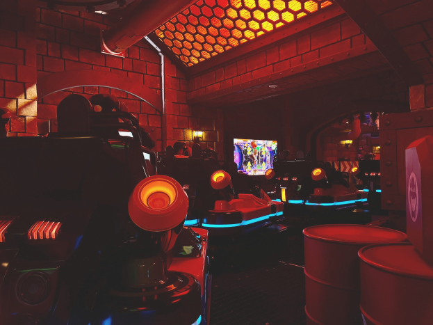 Ein hell erleuchteter Raum voller verschiedener Arcade-Videospielautomaten, Bildschirme und andere Ausrüstung, die eine lebendige Atmosphäre schaffen.