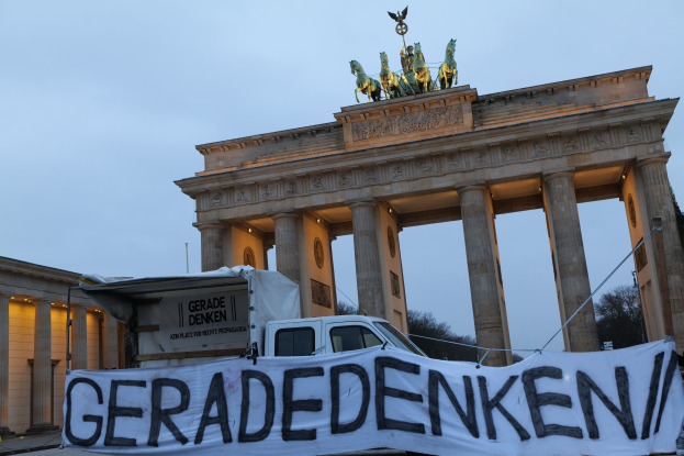 Ein Lkw steht vor dem Brandenburger Tor in Berlin, Deutschland, mit einer Fahne mit der Aufschrift "Geradedenken" in fetter Schrift, mit Statuen oben auf dem Tor und dem Himmel im Hintergrund.