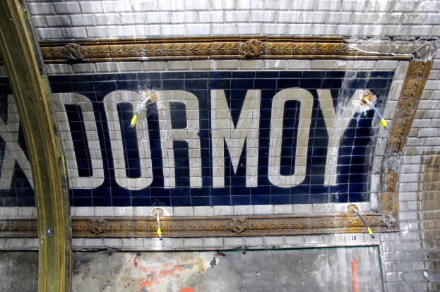 Eine U-Bahn-Station mit einem "Dormoy"-Schild an der Wand, einem Pfahl links und einer Tür unten.