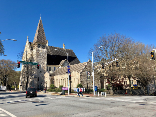 Die Episkopalkirche St. Lukas, eine große Kirche mit einem Turm, steht an einer Straßenecke umgeben von Gebäuden, Verkehr, Fußgängern und Grün unter einem klaren blauen Himmel.