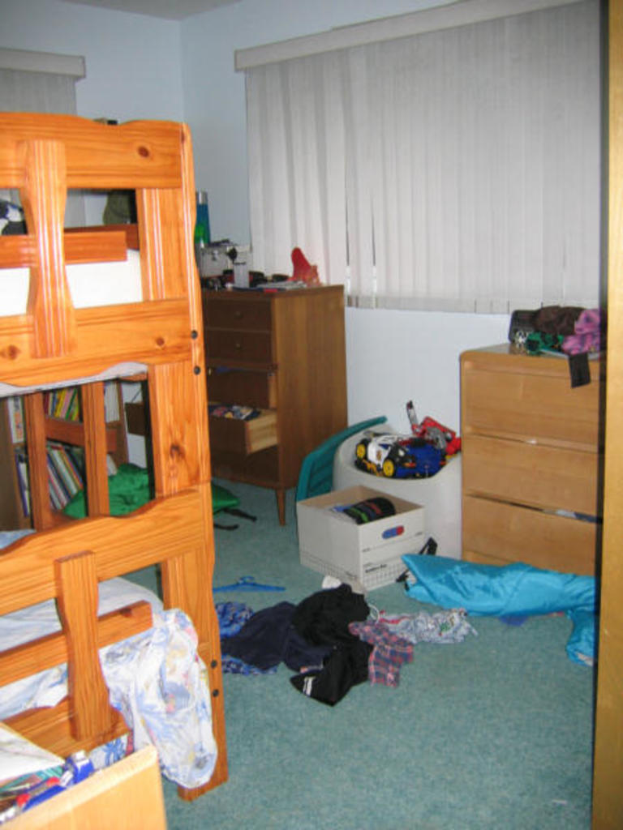 Ein Zimmer mit einem Doppelstockbett, Schreibtisch, Tisch und verstreuten Kleidern und Gegenständen auf dem Boden.