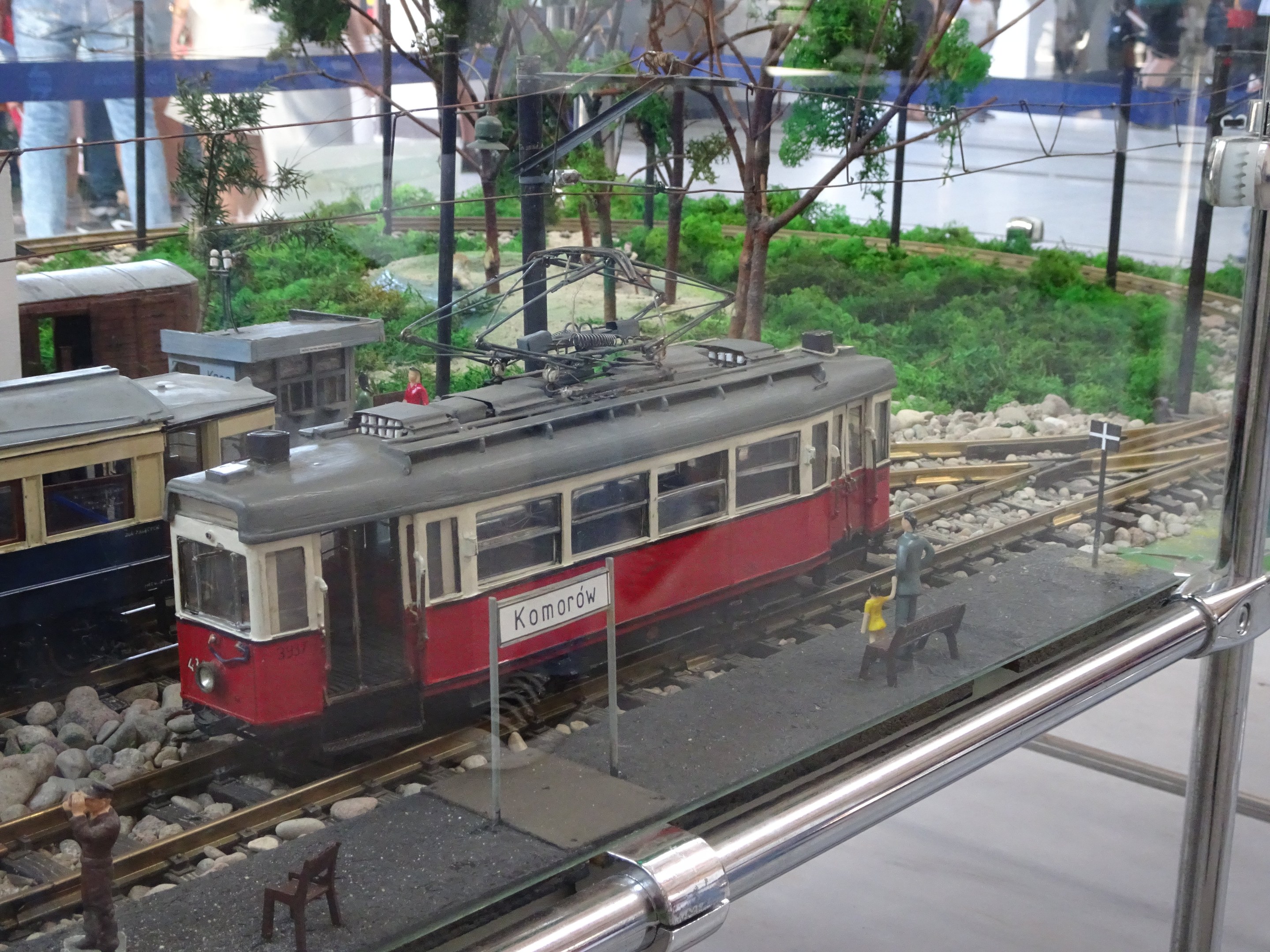Ein Modellzug in einer Glasvitrine mit Miniatur-Eisenbahnlandschaft und Zuschauern.