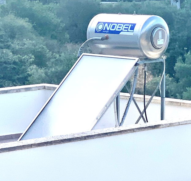 Solarwassererwärmer mit Speicher auf einem Gebäude installiert, Bäume im Hintergrund.