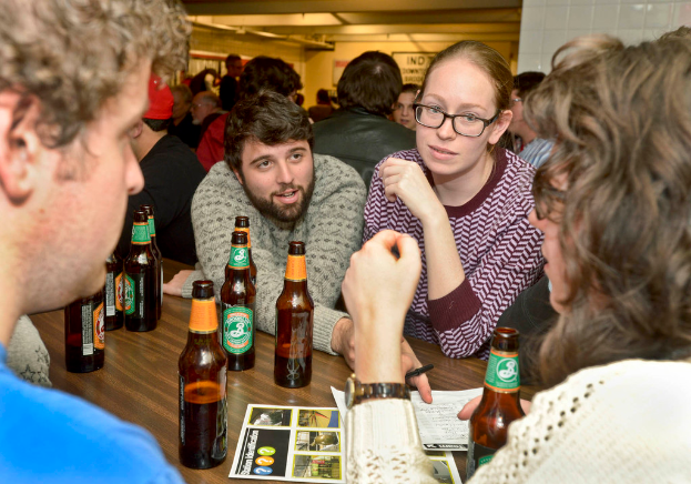 Mehrere Personen auf beiden Seiten eines Tisches mit Bierflaschen in einem scheinbar typischen Bar-Umfeld.