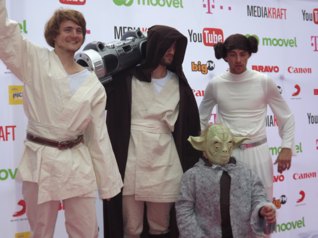 Gruppe von Menschen in Star-Wars-Kostümen, die auf einem roten Teppich posieren und ein Banner im Hintergrund halten.