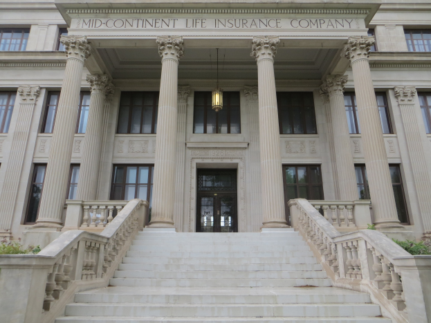 Großes Gebäude mit der Aufschrift "Mid-Continental Life Insurance Company", Fenstern, Säulen, einer Tür, einer Treppe mit Geländer und umliegenden Pflanzen.