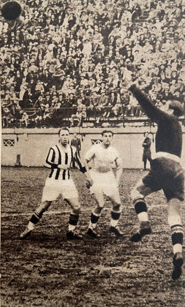 Ein Schwarz-Weiß-Foto einer Gruppe von Männern, die auf einem Feld Fußball spielen, mit einer Zuschauermenge im Hintergrund und einer Wand dahinter, mit dem Text "Newcastle United v West Bromwich Albion" unten.