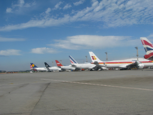 Eine Start- und Landebahn mit einigen Flugzeugen, Polen, Kabeln und Wolken am Himmel.