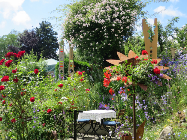 Ein Garten mit farbenfrohen Blumen und Pflanzen, der einen Tisch mit einer Decke und Stühlen zeigt, umgeben von Bäumen unter einem bewölkten Himmel auf der Chelsea Flower Show.