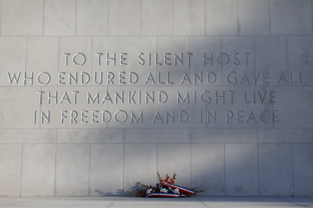Eine Gedenkwand mit einer Inschrift und einem Blumenstrauß davor.