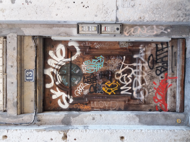 Eine alte Tür mit Graffiti in der Mitte eines Gebäudes, umgeben von einer Wand mit Rohren und verschiedenen Gegenständen, die herumliegen.