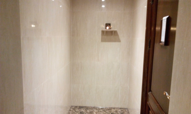 Badezimmer mit einer Duschwanne, Toilette und Tür auf der rechten Seite, mit Fliesen an den Wänden und Deckenleuchten.