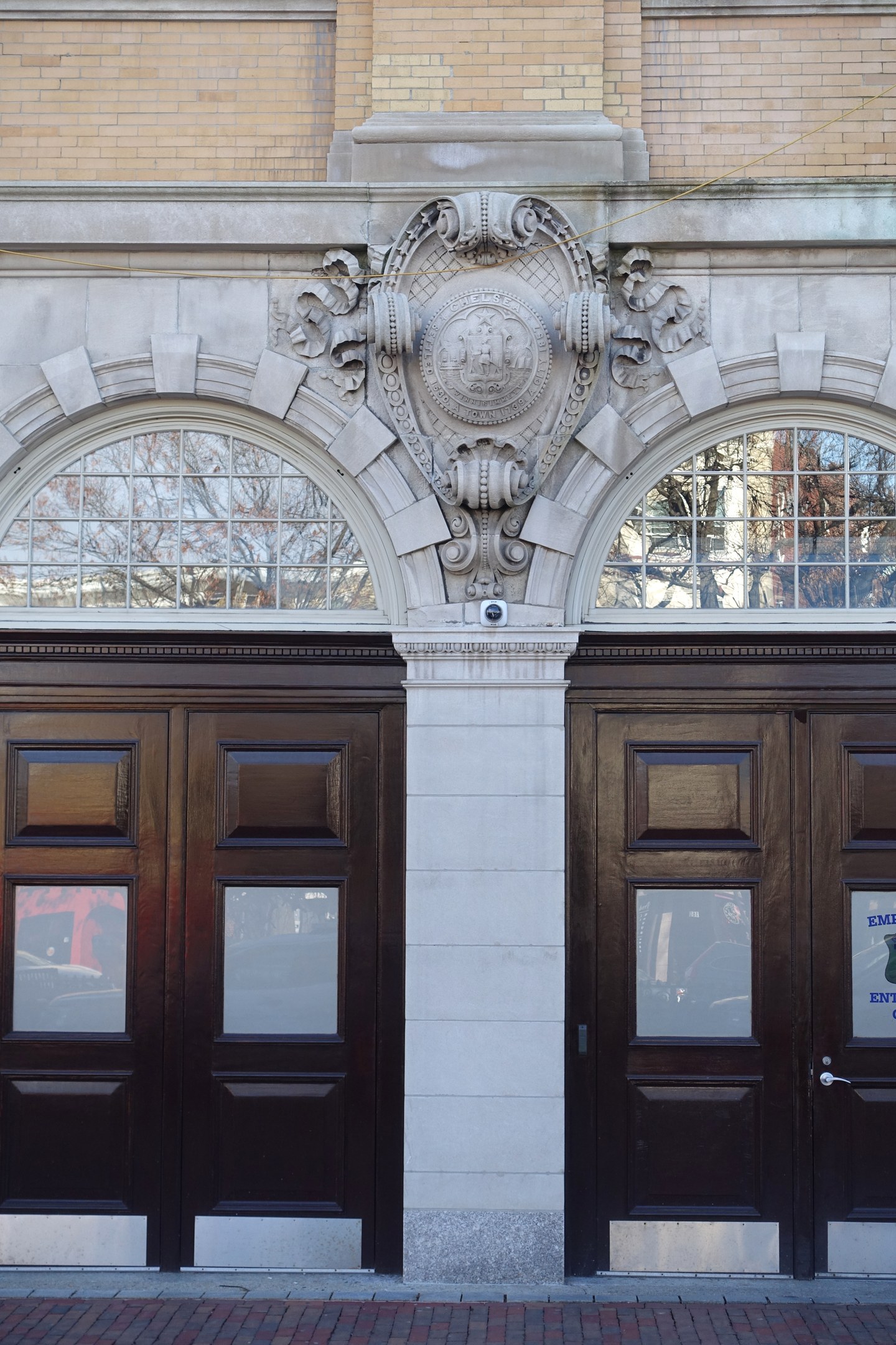 Zwei große hölzerne Türen mit Glasfenstern und Verzierungen an der Wand, erreichbar über einen Weg am unteren Bildrand.