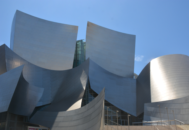 Das Künstler-Konzertgebäude in Los Angeles, ein modernes Gebäude mit Glaswänden, Treppen mit Geländern, die zur Eingangstür führen, umgeben von Laternenmasten, mit einer Tafel mit Text im Vordergrund und einem bewölkten Himmel im Hintergrund.