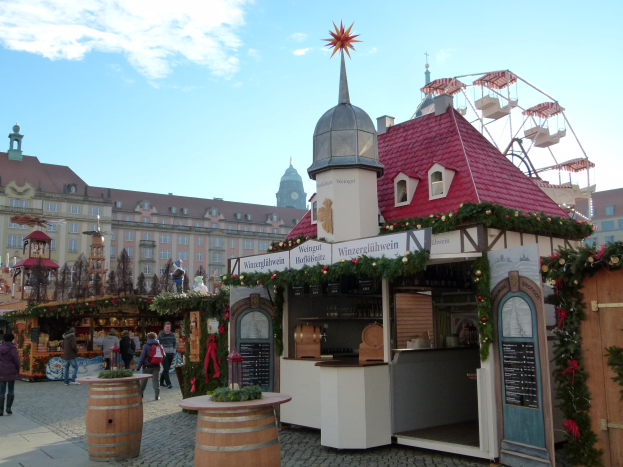 Ein geschäftiger Weihnachtsmarkt in Nürnberg, Deutschland mit Menschen um geschmückte Stände, festlicher Beleuchtung, einem Riesenrad, Gebäuden und einer Tafel mit Text auf der rechten Seite.