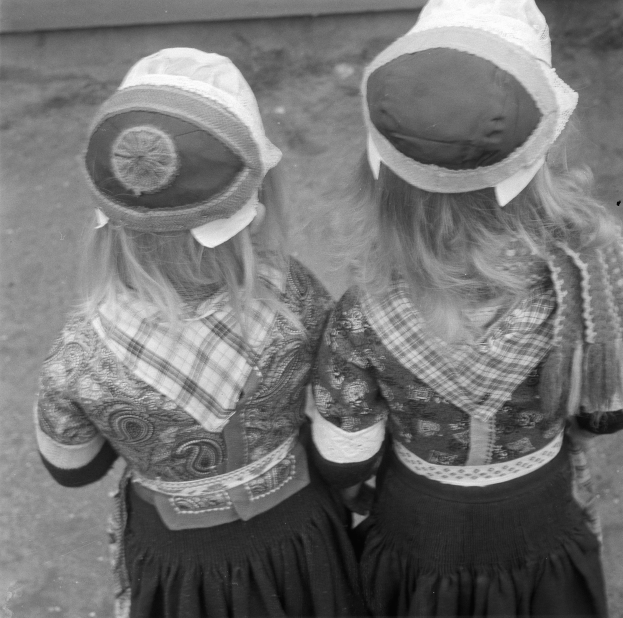 Zwei junge Mädchen in traditioneller bayrischer Tracht und Hüten stehen nebeneinander vor einer Wand, dargestellt in Schwarz-Weiß.