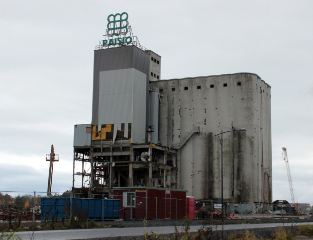 Großer Zementbau neben einer Straße mit umliegenden Pflanzen, Zaun, Polen, Laternen, gesetzt gegen Bäume und einen klaren blauen Himmel.