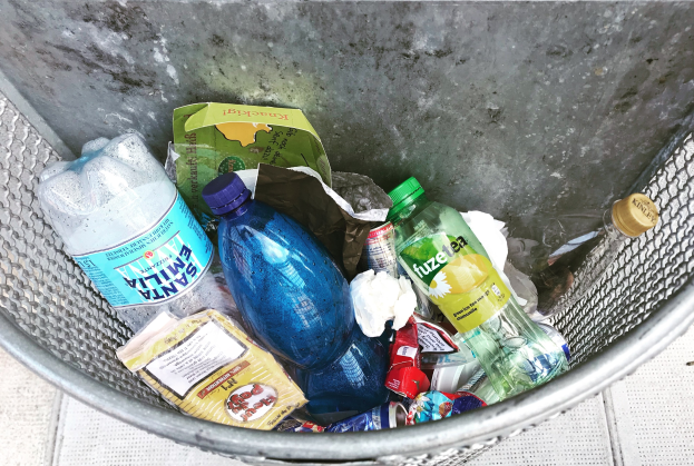 Ein Metallmüllcontainer voller Plastikflaschen, Beutel und anderer Abfallgegenstände.