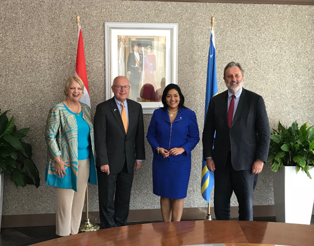 Eine Gruppe strahlender Menschen um einen Tisch mit Papieren herumstehend, umgeben von Fahnen, Topfpflanzen und einem Fotorahmen an der Wand, feiert die Unterzeichnung eines Memorandums von Verständigung zwischen den Vereinigten Staaten und Kanada.