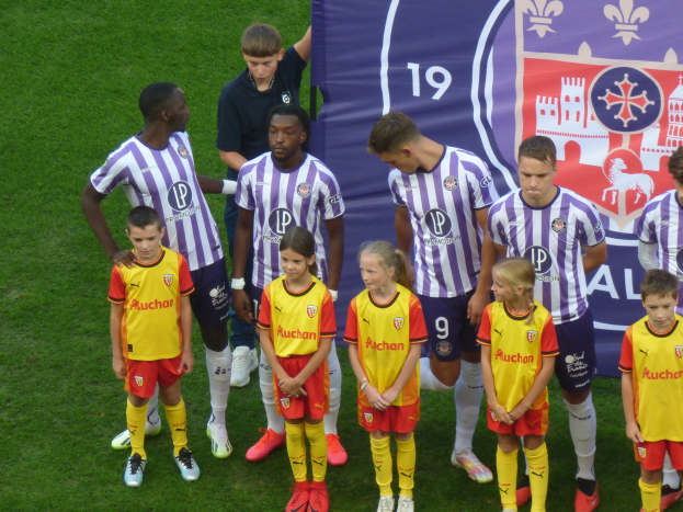 Gruppe junger Fußballspieler auf einem grünen Feld mit einem "Ligue 1"-Banner im Hintergrund.