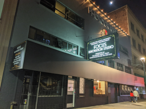 Außenansicht des Focus Innovation Studio in New York City bei Nacht, mit beleuchteten Gebäuden, Menschen auf dem Gehweg und sichtbarem Himmel im Hintergrund.