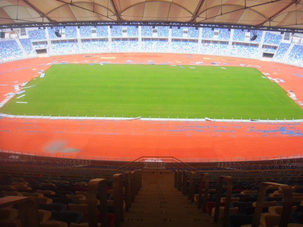 Großes Stadion mit vielen Zuschauern, mit Terrassen, Geländern, Treppen und Dach, mit dem Spielfeld in der Mitte sichtbar.