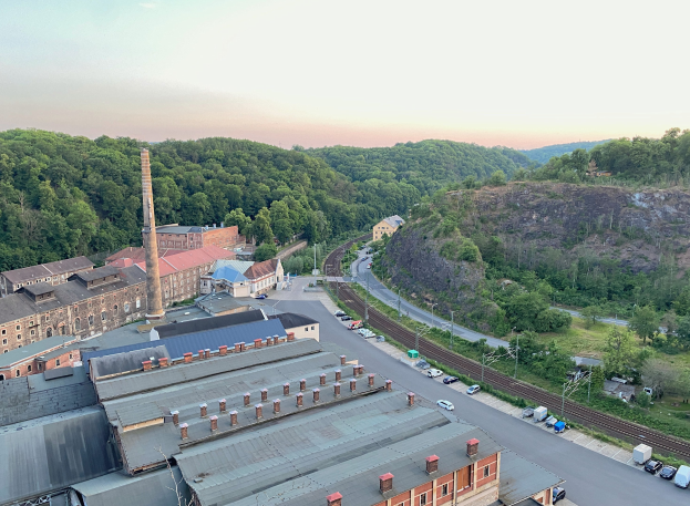 Luftaufnahme einer Stadt mit dichtem Gebäudebestand, befahrenen Straßen, Strommasten, vereinzelten Bäumen, fernen Hügeln und einem bewölkten Himmel, ähnlich einem Kohlebergbaugebiet.