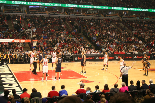 Eine Gruppe von Menschen in einem Stadion, einige halten einen Basketball, andere schauen von den Rängen und Werbung ist auf den Anzeigetafeln zu sehen.
