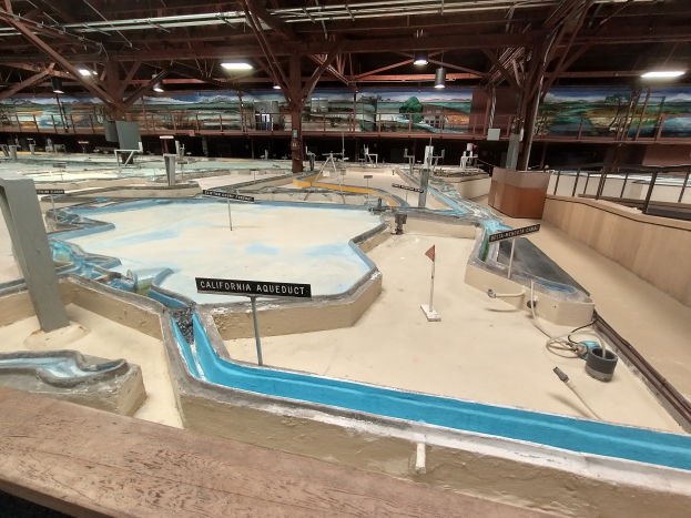 Ein großes Indoor-Wasserpark mit zahlreichen Wasserrutschen, Pfosten, Beschilderung, Deckenleuchten und Wandgemälde, das einem Minigolfplatz ähnelt.