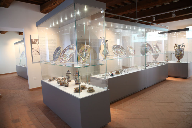 Ein Raum voller Glasvitrinen mit Keramikobjekten wie Tellern, Tassen, Untertassen und Vasen, beleuchtet von Deckenlampen, mit einer Informationswand auf der linken Seite, die sich auf die Ausstellung "Die Kunst der Keramik" im Museum of Fine Arts in San Francisco, Kalifornien bezieht.