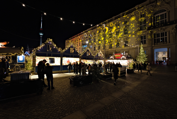 Ein lebendiger Weihnachtsmarkt in Berlin, Deutschland, mit Menschen um beleuchtete Stände, festliche Dekorationen und Gebäude mit erleuchteten Fenstern unter einem dunklen Himmel.