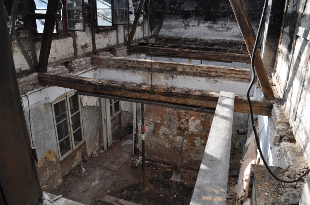 Ein Innenblick in ein Gebäude mit Schutt auf dem Boden, einschließlich zerbrochener Fenster, Holzpfosten, Drähte und verschiedenen anderen Gegenständen.