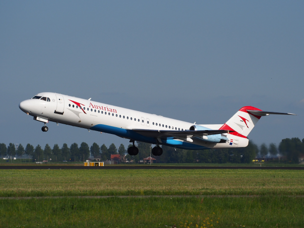 Austrian Airlines Embraer ERJ-190 Flugzeug beim Abheben vom Frankfurter Flughafen, mit grünem Gras darunter, Bäumen und Gebäuden im Hintergrund und Himmel darüber.