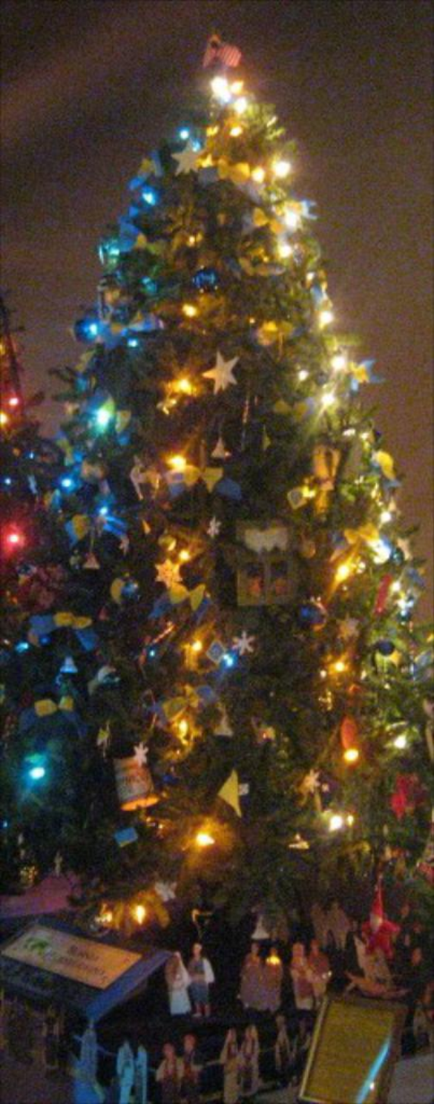 Ein geschmückter Weihnachtsbaum mit Menschenstatuen auf einem darunter liegenden Tisch.
