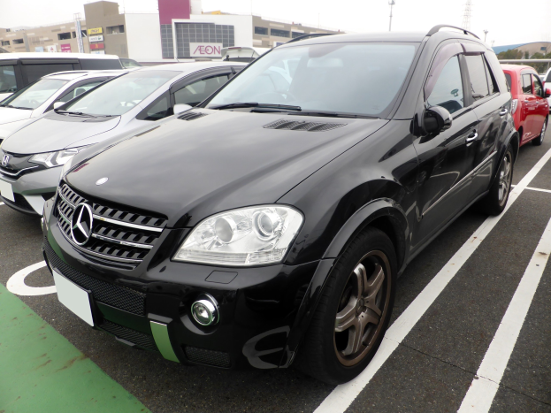Schwarzer Mercedes-Benz ML 350 CDI BlueEfficiency auf einem Parkplatz mit Gebäuden, Masten, Bäumen und einem klaren blauen Himmel.