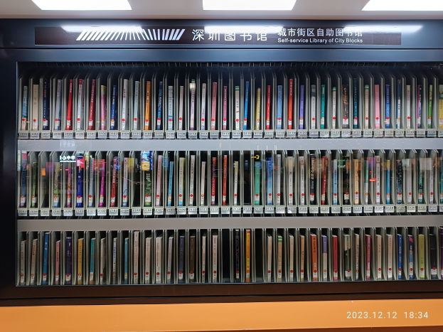 Eine gut beleuchtete Bibliothek mit hohen Bücherregalen voller Bücher, ein sichtbares Textbrett und ein Wasserzeichen unten, das an eine Selbstbedienungsbibliothek in Stadtblocks erinnert.