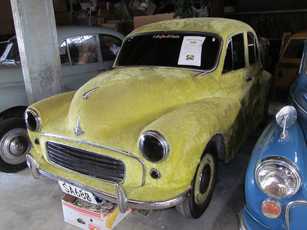 Eine Reihe von Oldtimern vor einer Wand mit verschiedenen Zubehörteilen geparkt, mit einer Säule auf der linken Seite.