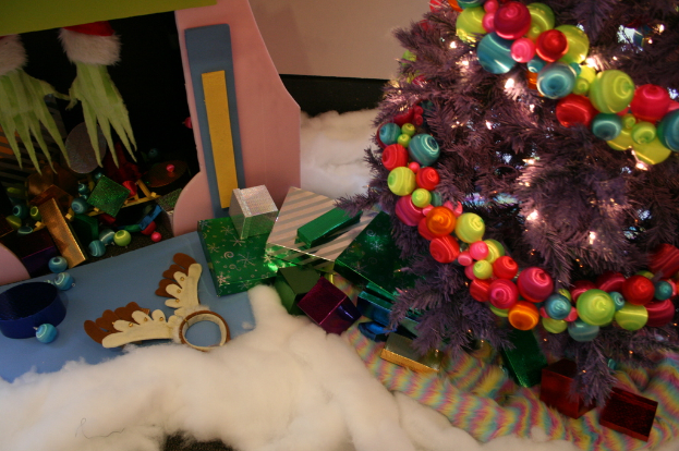 Innenansicht: Dekorierter Weihnachtsbaum rechts, Geschenkboxen und Dekorationen in der Mitte, Hütte mit Dekorationen oben links und Baumwolle und Wolle unten.