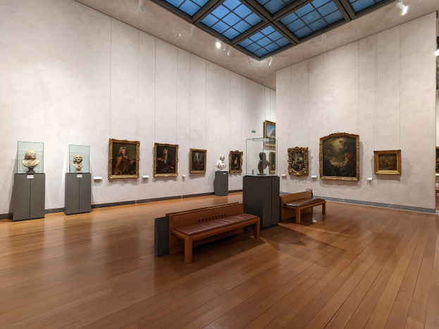 Ein geräumiger Raum im Metropolitan Museum of Art in New York City, der zahlreiche Gemälde an den Wänden, Bänke auf dem Boden, Statuen auf Ständern und Lampen an der Decke aufweist.