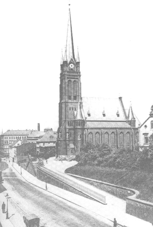 Schwarzes und weißes Foto einer Stadtstraße mit der St. Peter Kirche in Wiesbaden im Hintergrund, flankiert von Gebäuden, Bäumen, Fahrzeugen und Passanten.