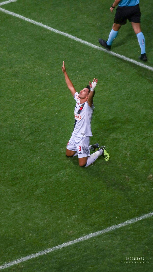 Ein Fußballspieler in Uniform kniet auf dem Feld mit ausgestreckten Armen in Feier.
