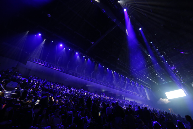 Große Menschenmenge auf Sitzplätzen und Stehplätzen in einem Stadion mit Geländern, Zelten und Überdachung während eines Events in der O2 Arena in London.