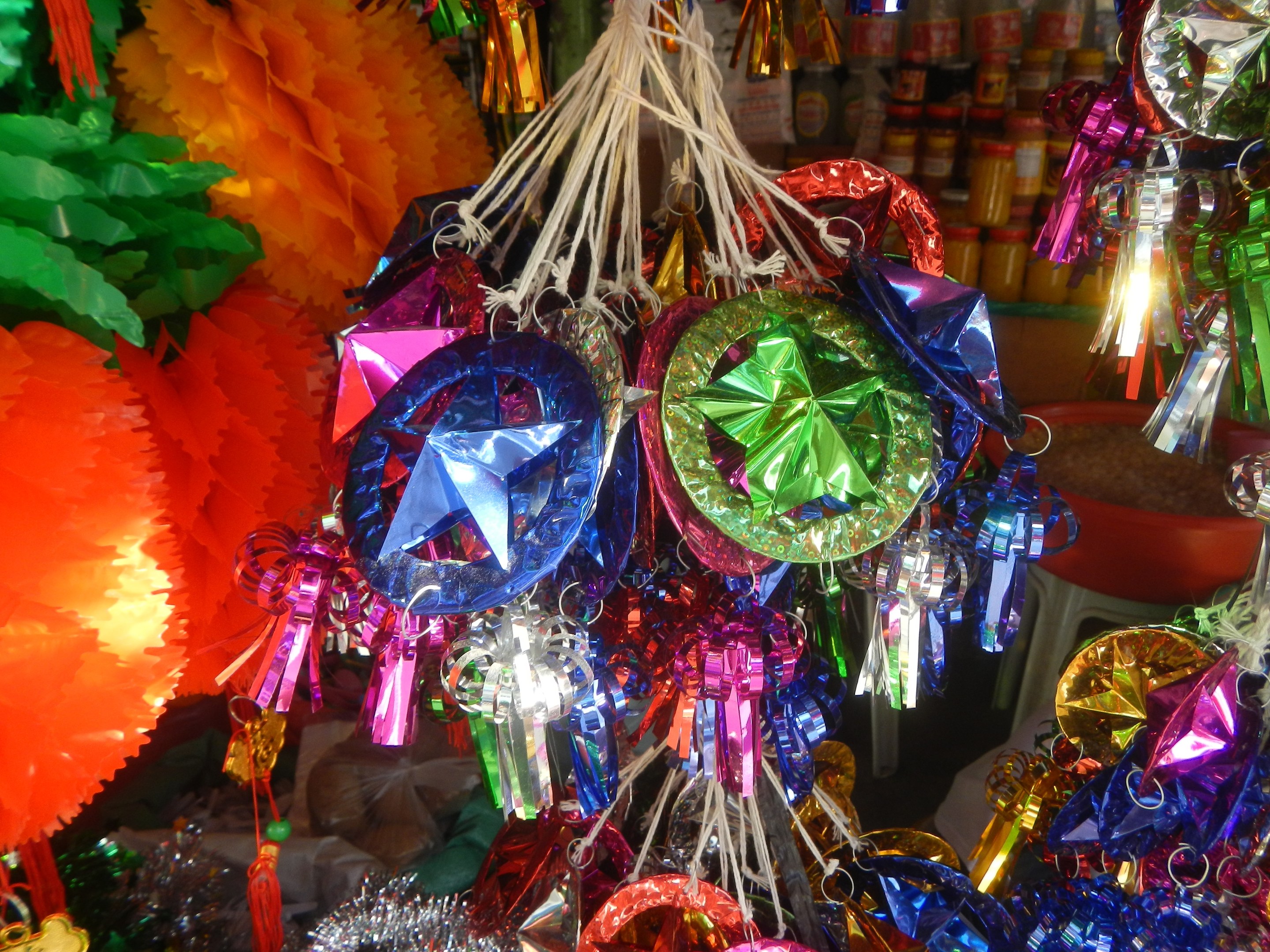 Farbenfrohe Dekorationen wie Laternen und Bänder hängen von der Decke über Regalen voller Flaschen in einer festlichen Atmosphäre.
